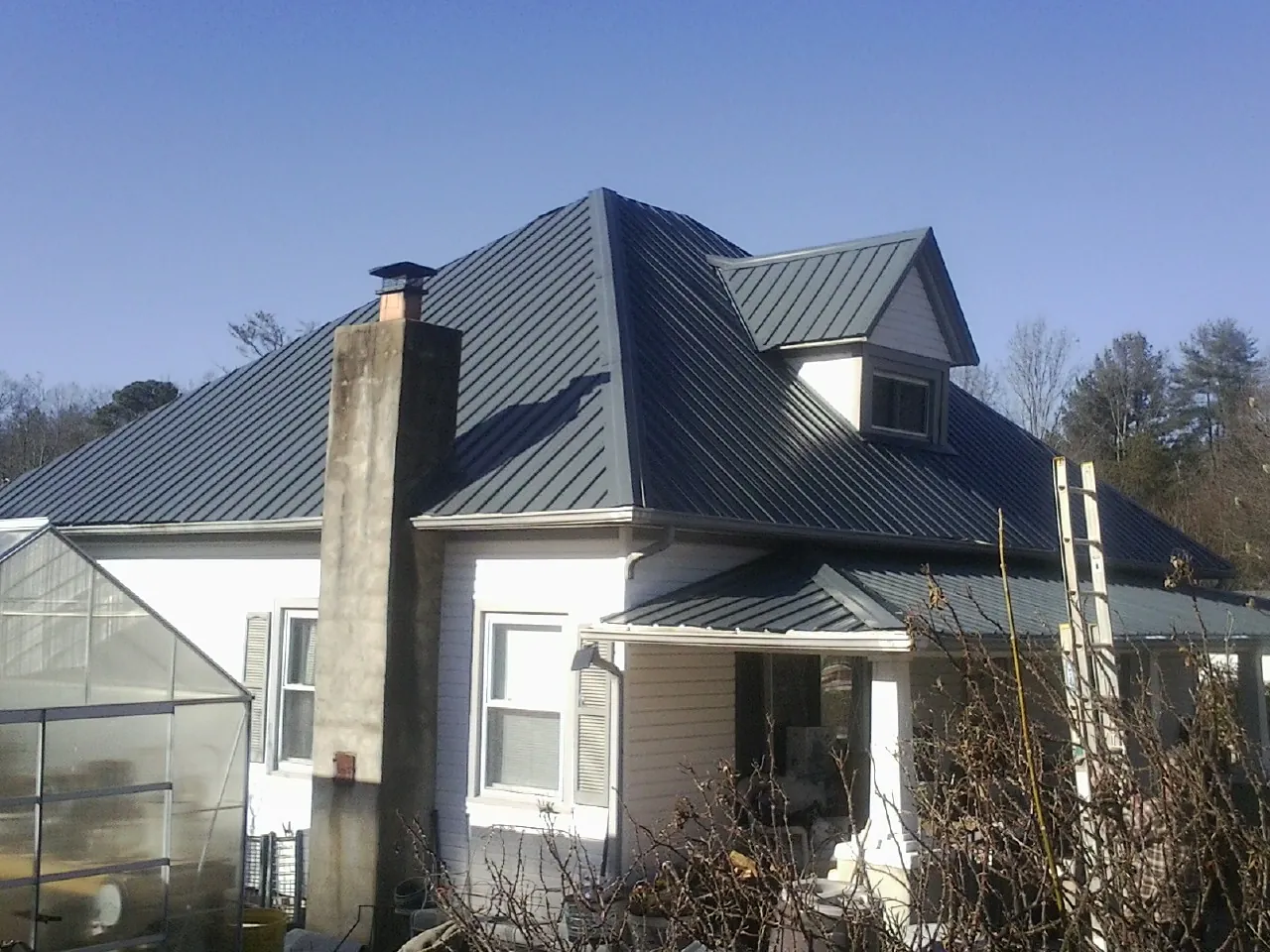 Dark blue standing seam metal roof on a white farmhouse with dormer — Slate & Tile Roof Repair by Roofing Brothers in Gloverville