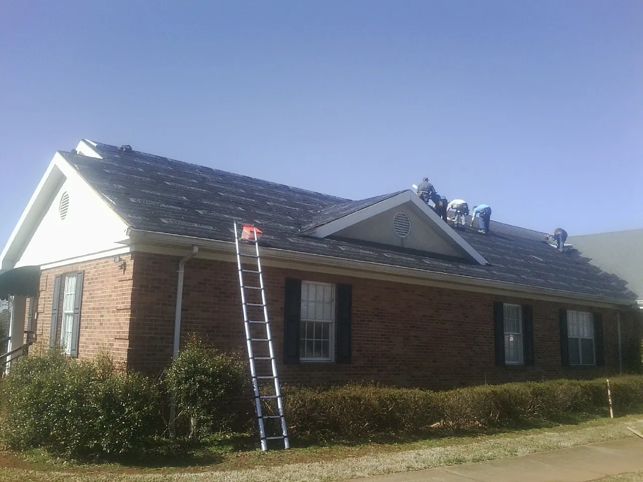 Crew tearing shingles off a brick ranch roof with a ladder set — Emergency Roof Repair work by our crew in Gloverville