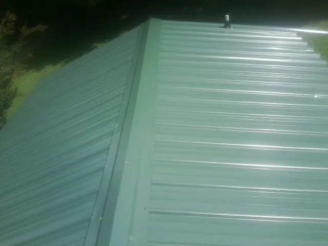 New green metal panels meeting at the ridge of a roof — Flat Roof Repair work by our crew in Gloverville
