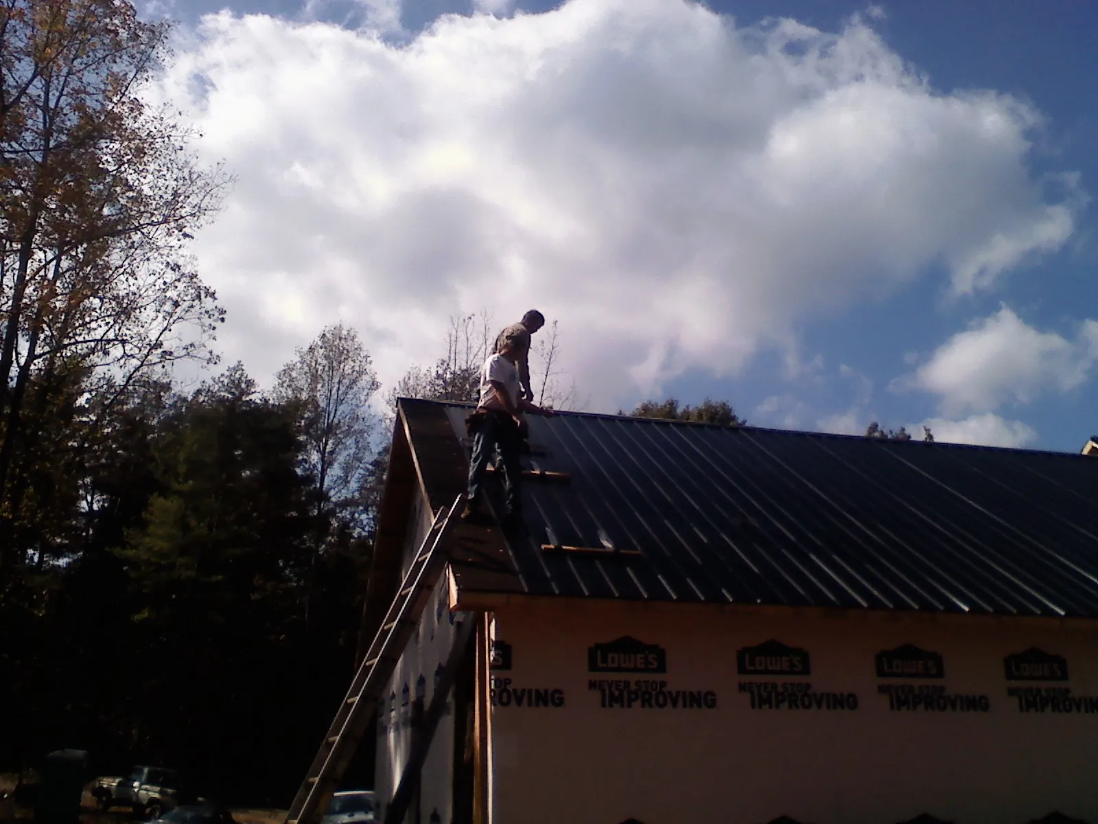 Roofer fastening dark metal panels high against a cloudy sky, from a Roof Inspection job in Gloverville