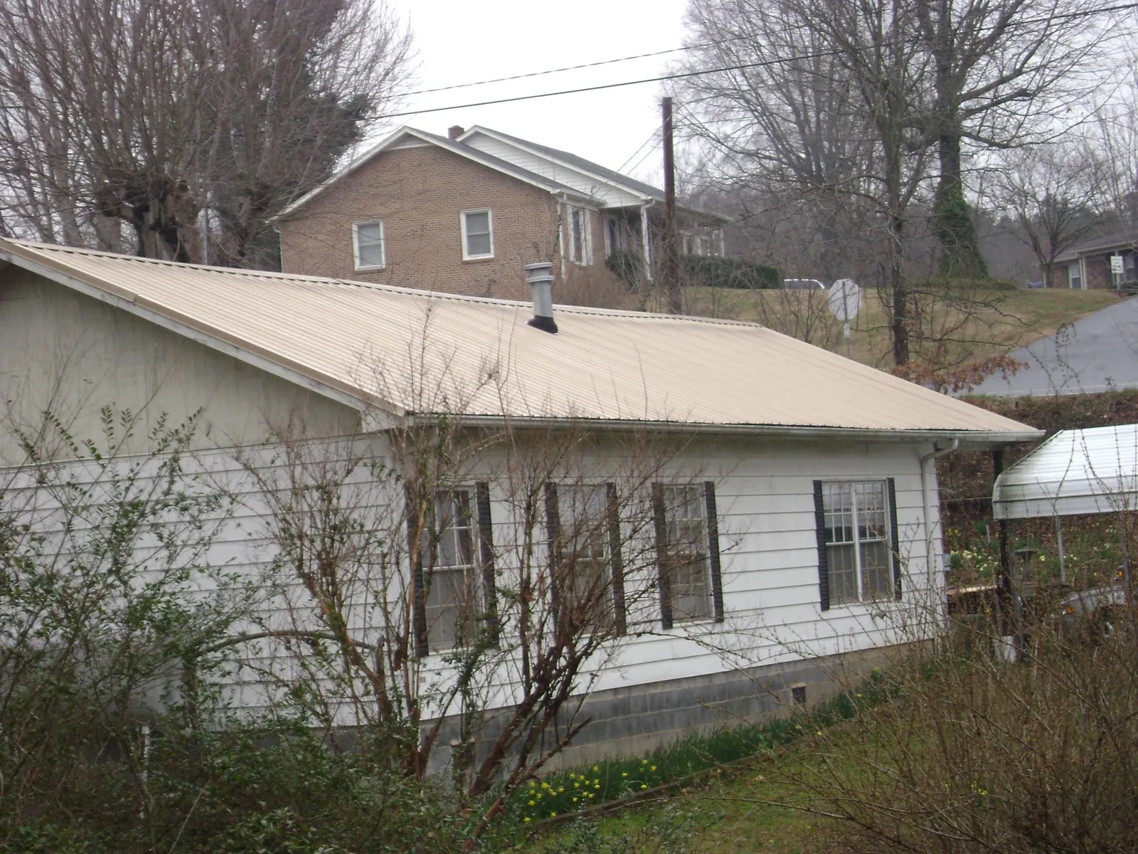 Tan metal roof on a white sided house set into a hillside — Commercial Roofing by Roofing Brothers in Gloverville