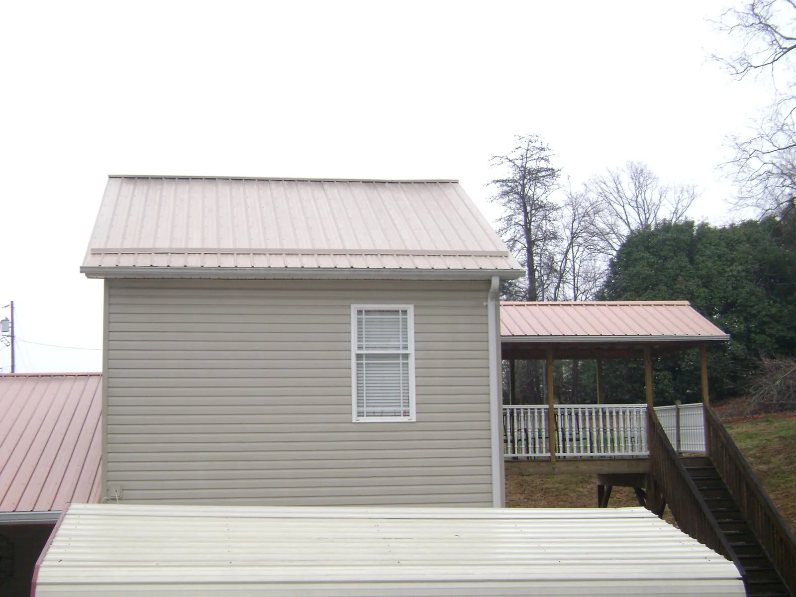 Tan metal roofs on a two story addition and attached porch, from a Roof Replacement job in Gloverville
